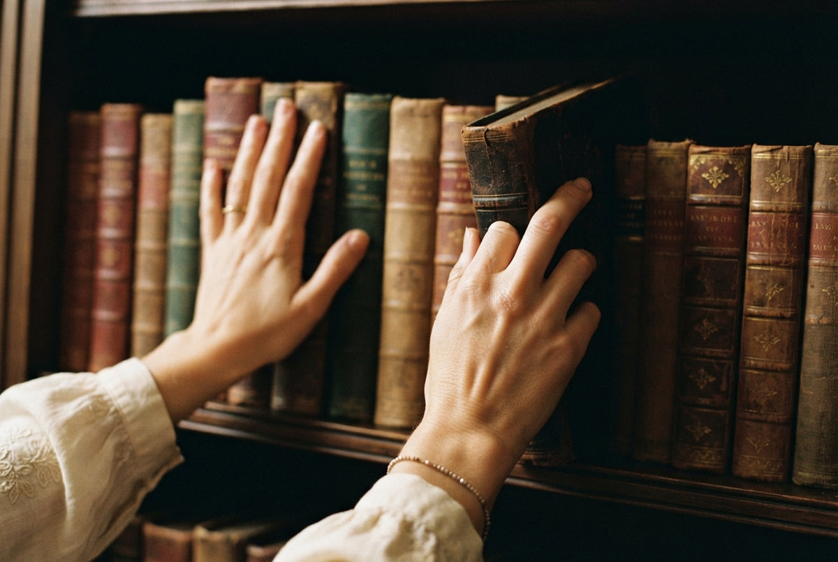 A pair of hands drawing an old leather-bound book from a shelf of antique books