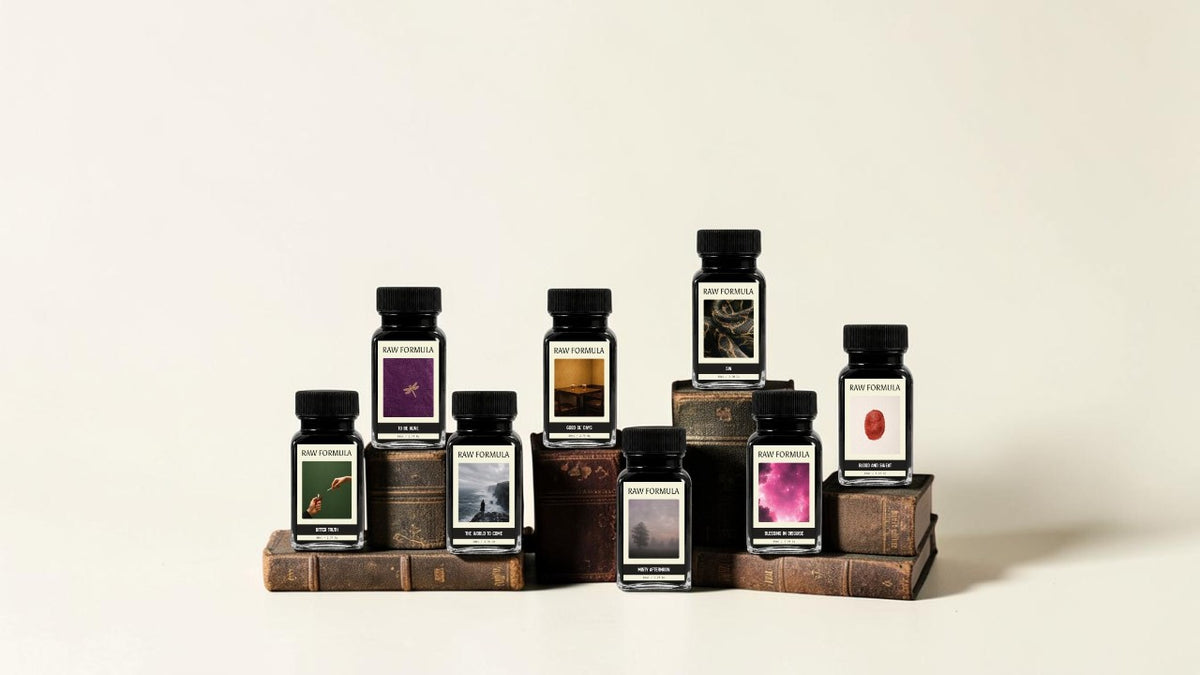 The eight Raw Formula fountain pen ink bottles from the Formula of Life collection, arranged on antique books