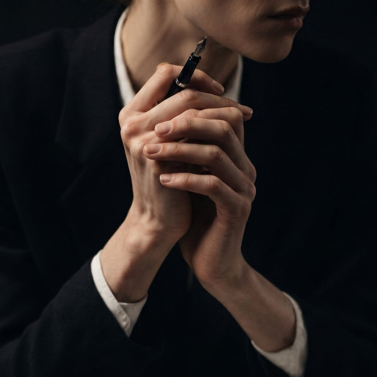 A person holding a fountain pen with both hands clasped, pausing in thought